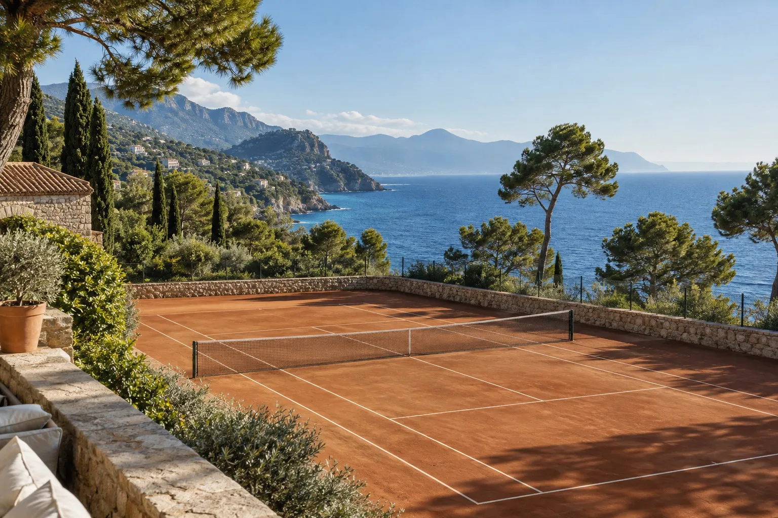 A clay tennis court overlooking a Mediterranean coastline.